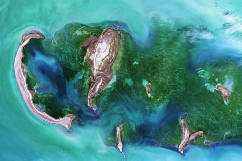 Satellite image of the Tyuleniy Archipelago, Kazakhstan: in greens and browns against bright waters in swirls of blue