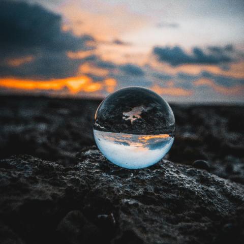 A reflective glass sphere placed on a rough, rocky surface at sunset